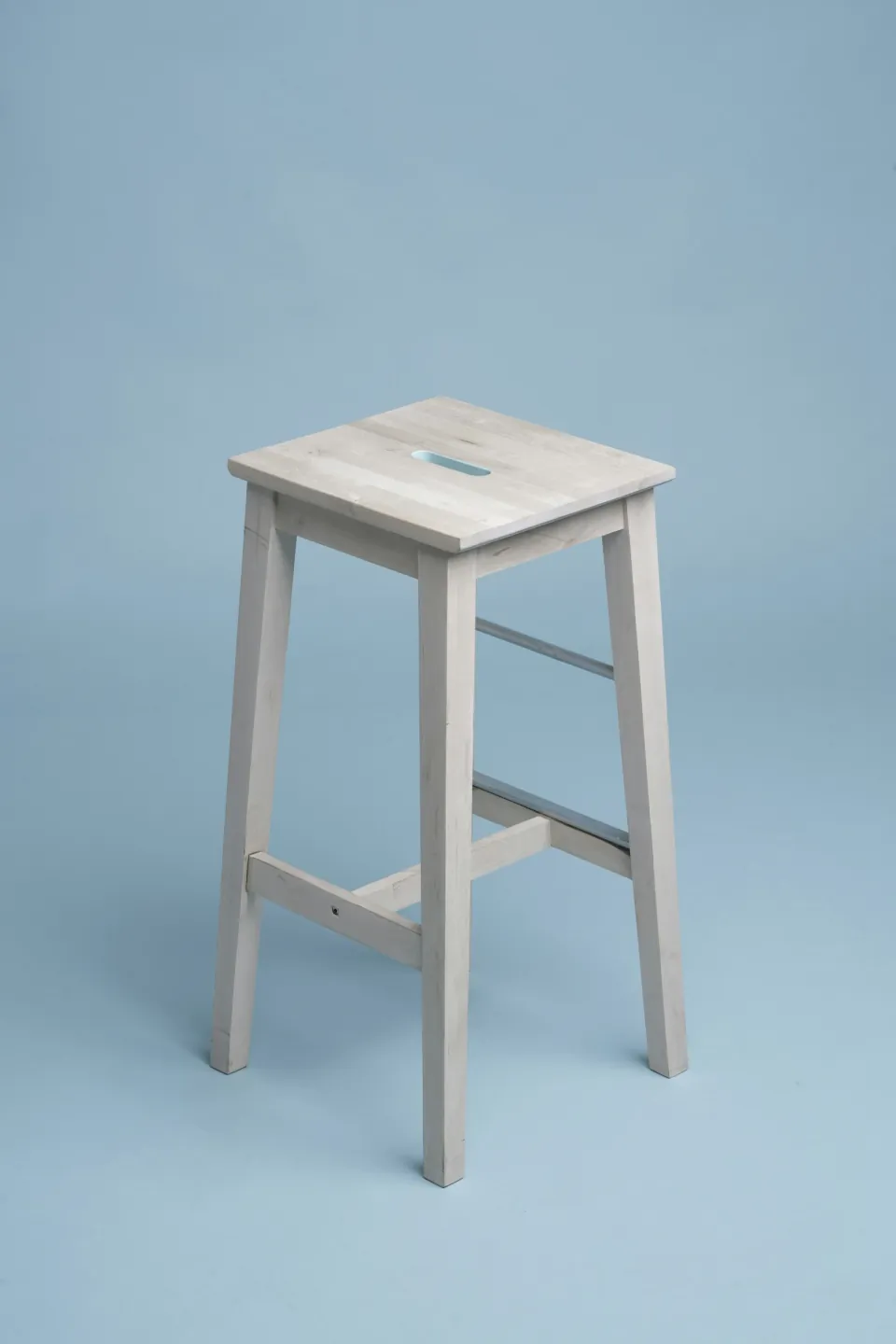 White wooden stool photographed on a light blue studio background